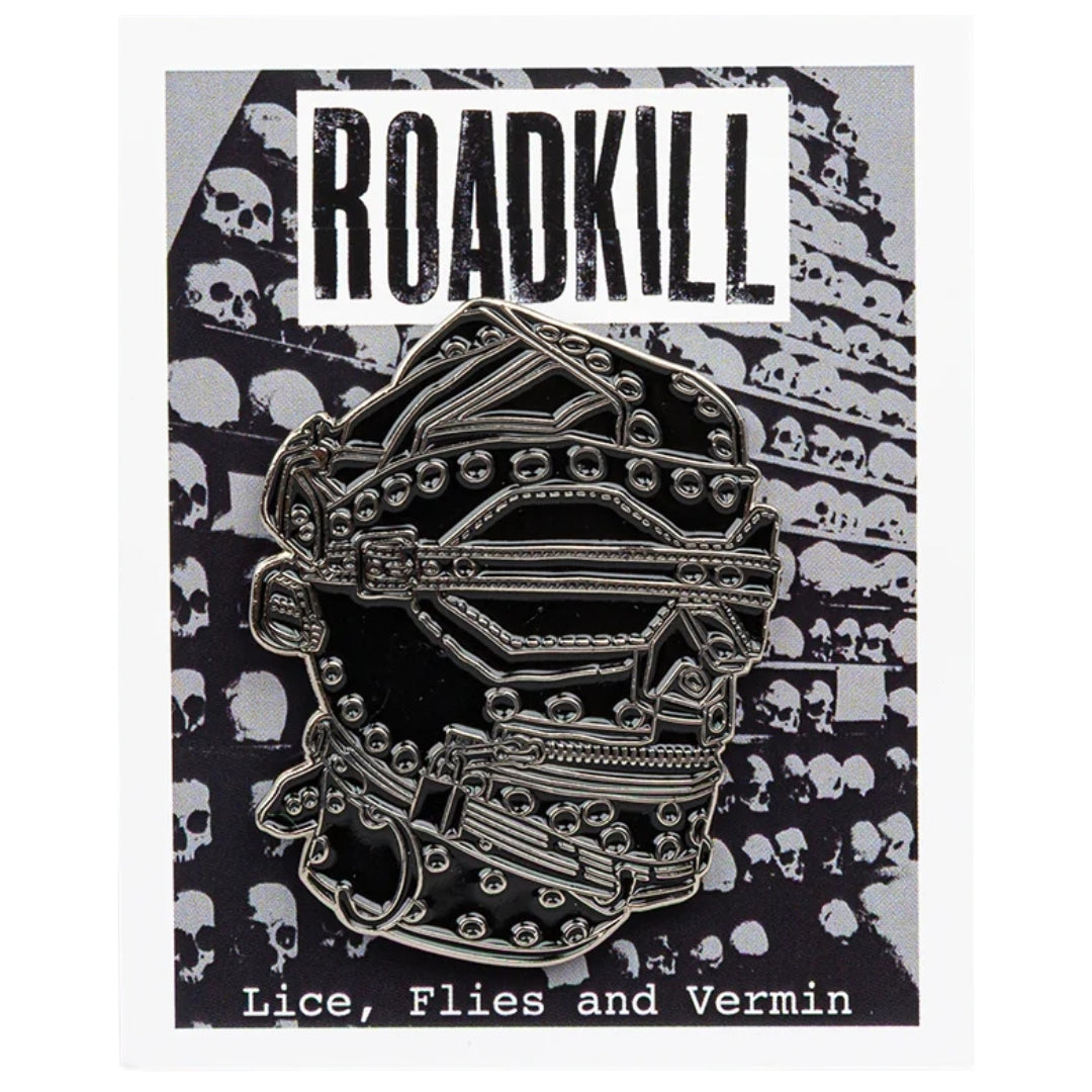 Metallic skull pin with 'Roadkill' branding on a black and white patterned background