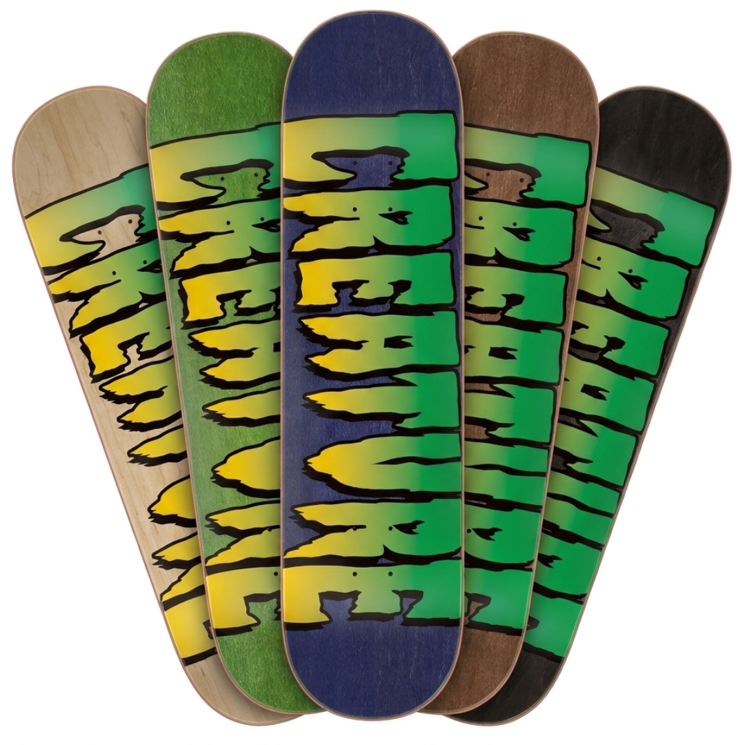Five skateboard decks fanned out against a white background, each showing a different natural wood tone and a bold green and yellow graphic with black outline.
