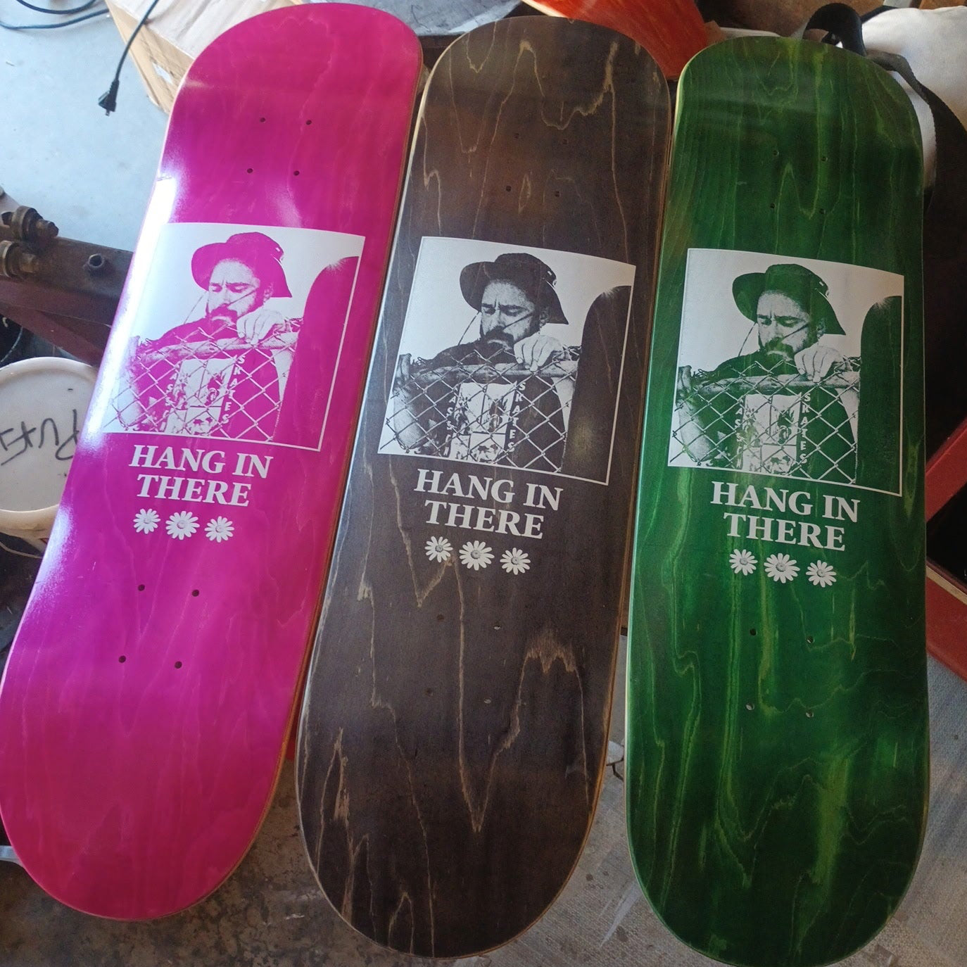 Three skateboard decks with 'Hang In There' text and images on a workshop background.