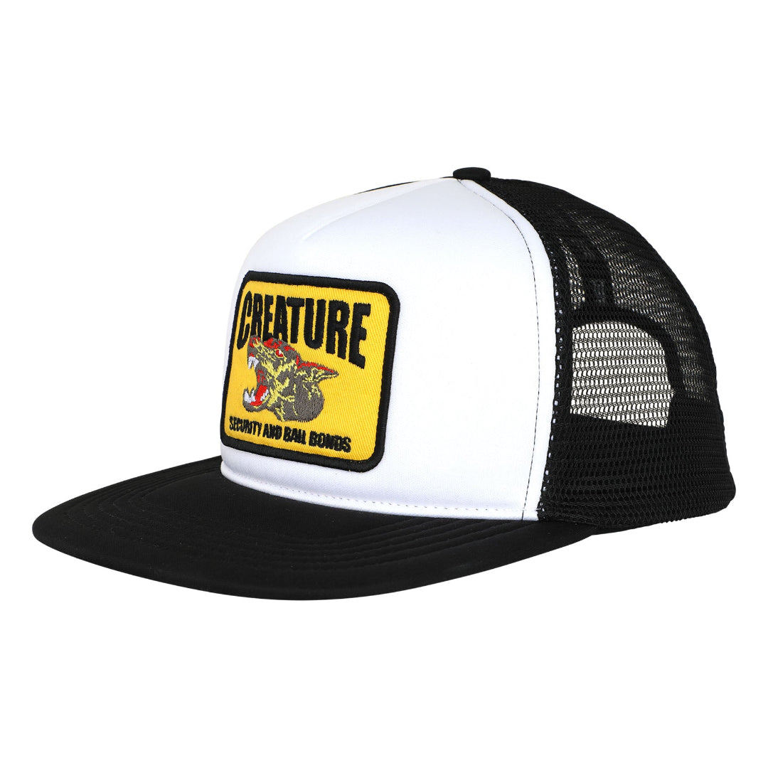 A black and white trucker hat featuring a yellow rectangular patch on the front with the brand name 'CREATURE SECURITY AND BALL BONDS' and a graphic of a motorcycle.