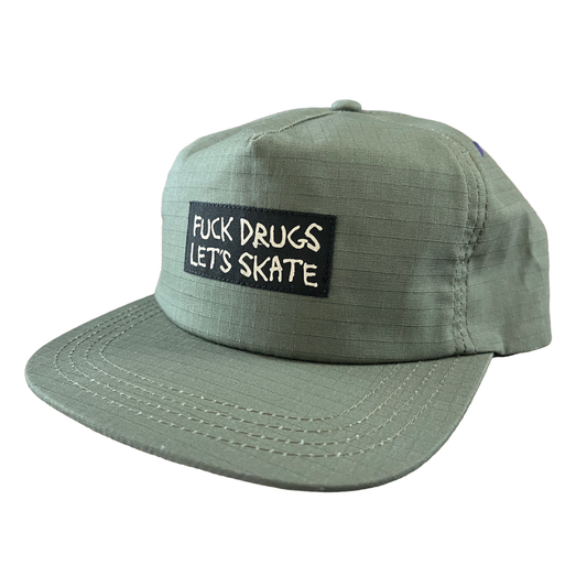 An olive green flat-brim cap with a black rectangular patch on the front that reads 'FUCK DRUGS LET'S SKATE' in white text, shown on a plain white background.