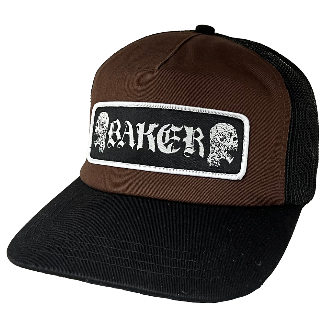A brown and black trucker hat with a rectangular front patch featuring the word 'BAKER' in white gothic lettering between two white skulls, shown on a plain white background.