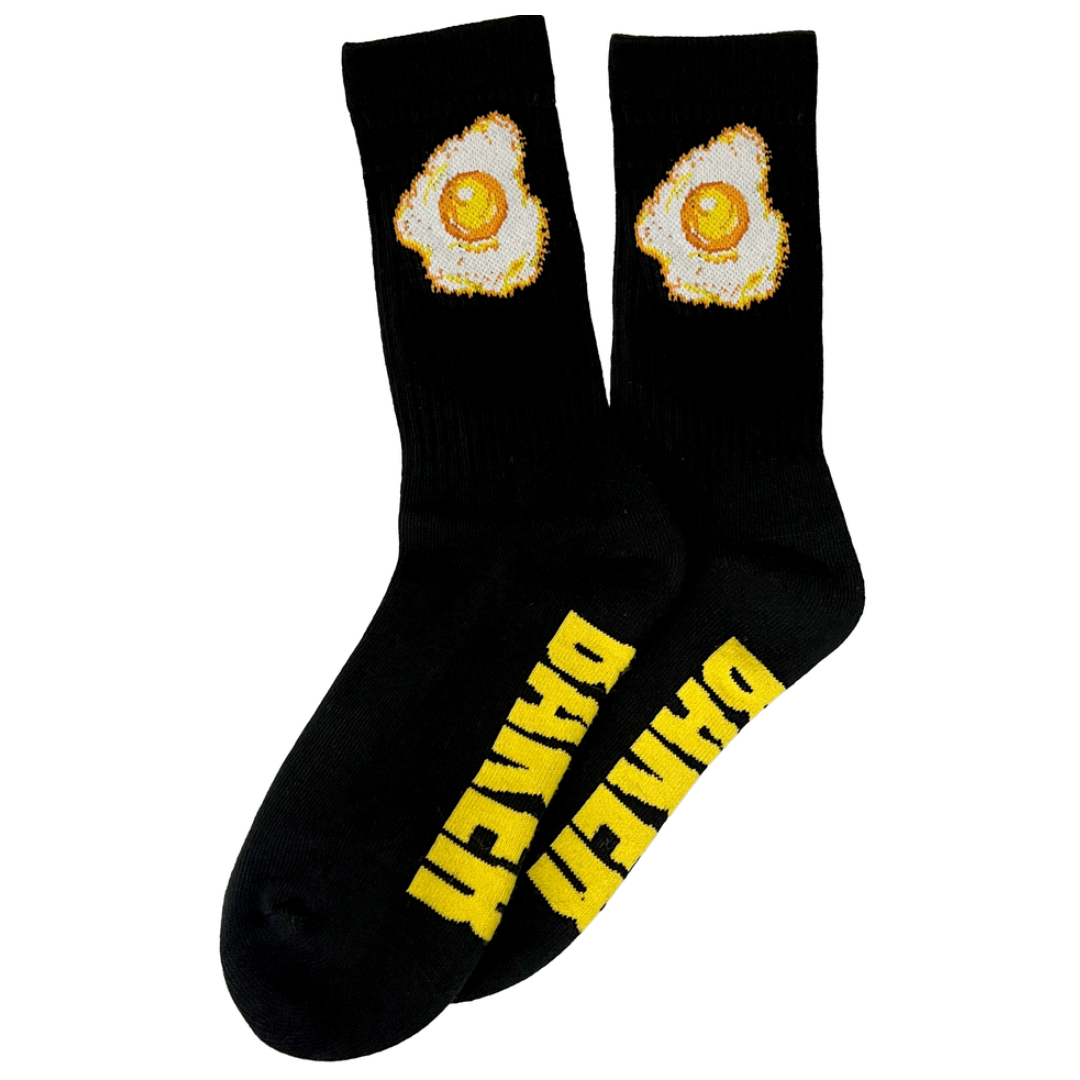 A pair of black crew socks featuring a graphic of two fried eggs on the upper cuff and the word 'DRIVEN' printed in bold yellow letters along the side of the foot.