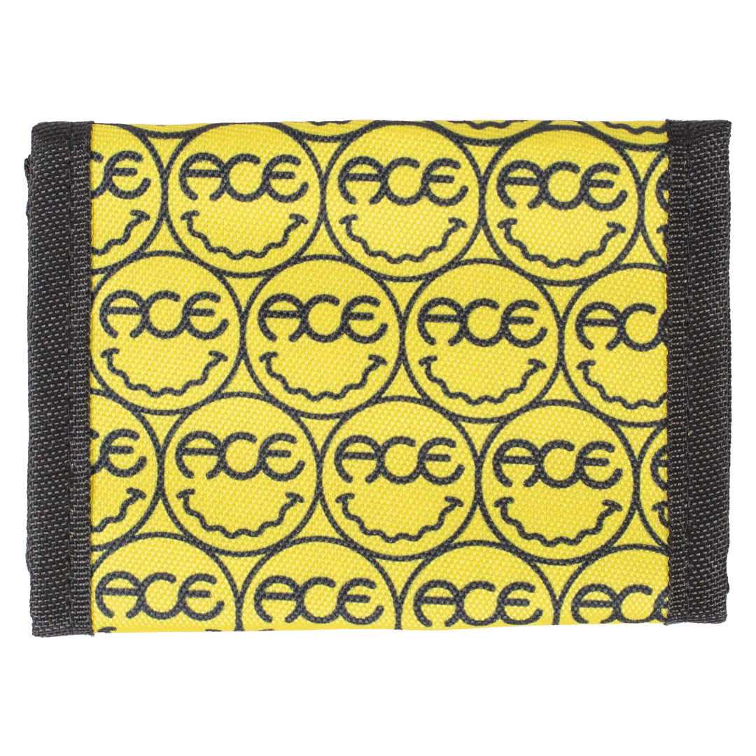 A yellow fabric wallet featuring a repeating pattern of black smiley faces inside circles with the text 'FACE' integrated into each smiley. The wallet has black webbed side panels on a plain white background.