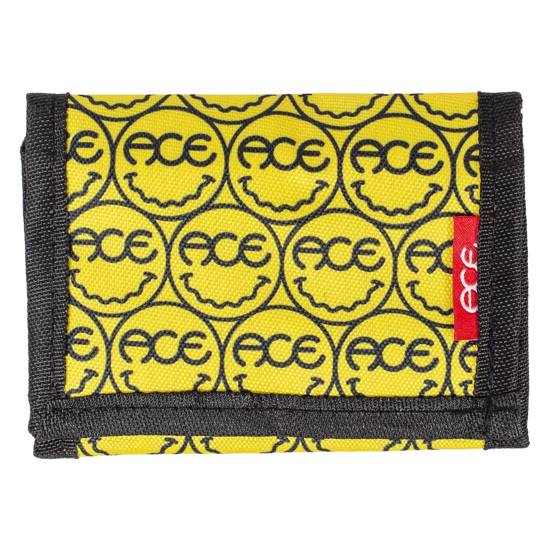 A yellow fabric wallet with a repeating black smiley face pattern containing the brand name 'FACE' and a red side tab with 'ACE' in white text, shown on a plain white background.